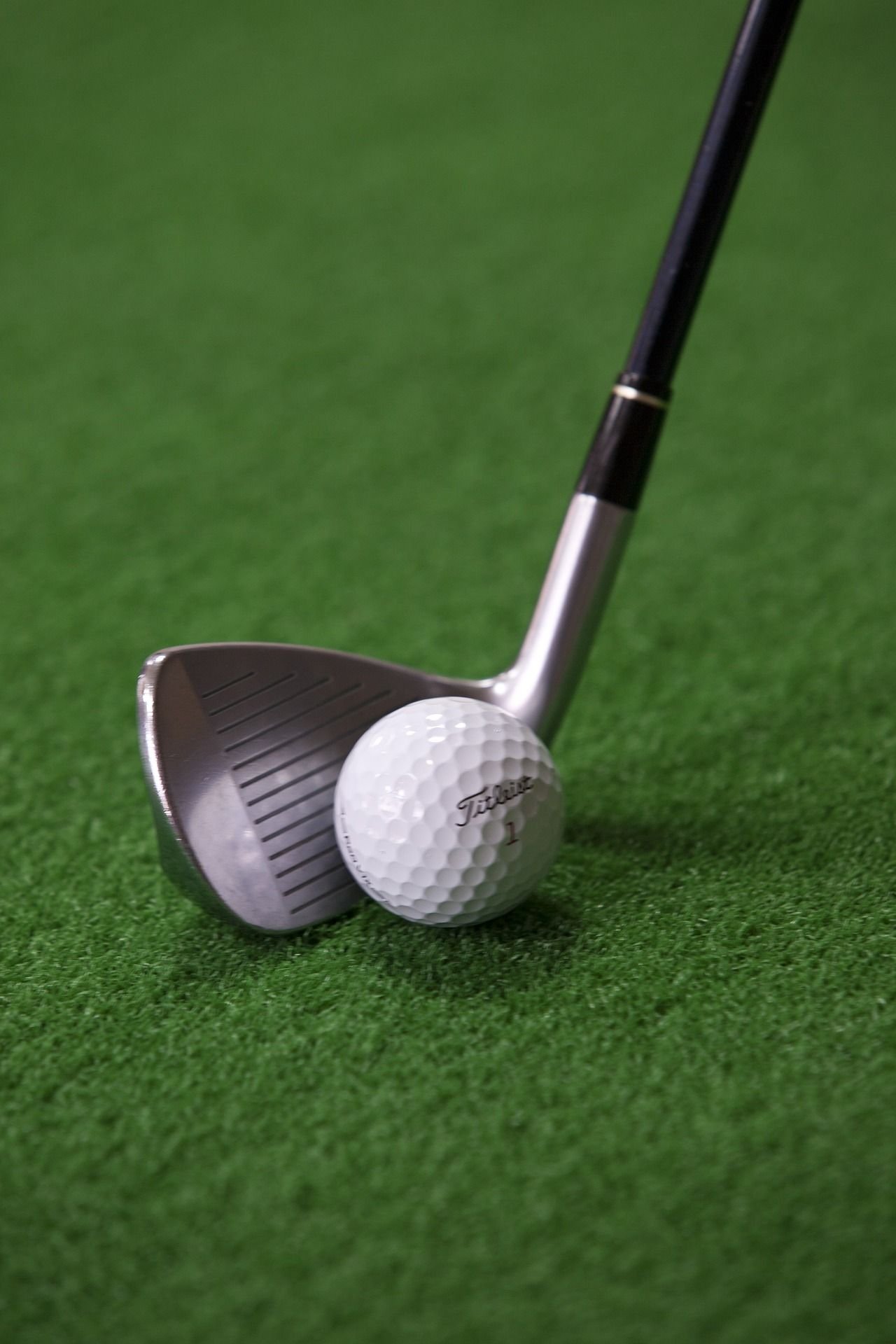 Close-up of a golf club next to a white golf ball on a green turf, resembling the pristine putting greens often seen in Tampa, FL. The club is positioned as if about to strike the ball. The textured surface of the golf ball and the metallic finish of the club are clearly visible.